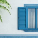 Volet aluminium teinté bleu sur façade maison blanche et palmier